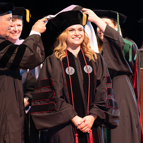 Dental student in convocation gown smiling as she is flanked by two individuals.