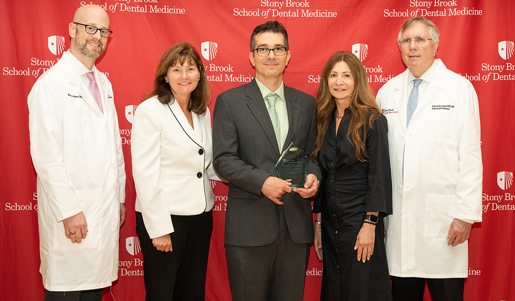 Award recipient Greg Maddalena (middle) flanked by school administration in front of dental school branded drapery
