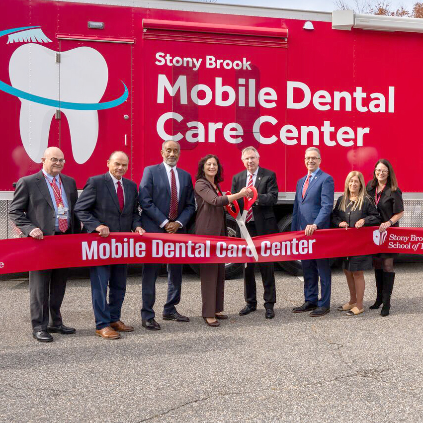 Administrators, faculty and staff cutting a ribbon in front of the new Mobile Dental Care Center