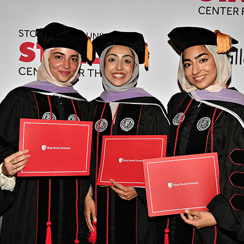 Three graduates in cap and gown holding their dental school diplomas