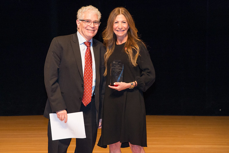 Dr. Ralph Epstein (left) and Dr. Stacy Reisfeld (right) on stage at the Staller Center for the Arts. Dr. Stacy Reisfeld holds an award to present to Dr. Epstein.