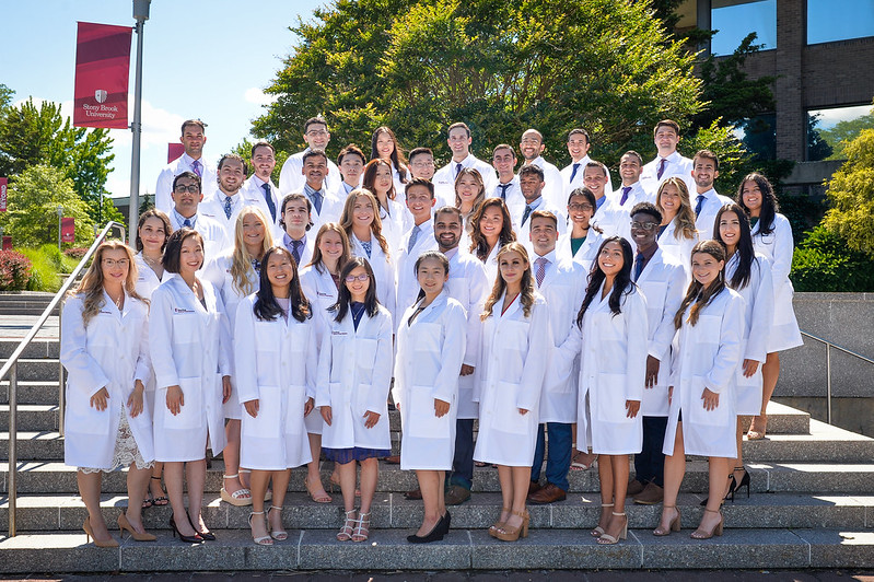 A group photo of Stony Brook University School of Dental Medicine's Class of 2023 wearing their white clinical coats.A group photo of Stony Brook University School of Dental Medicine's Class of 2023 wearing their white clinical coats.