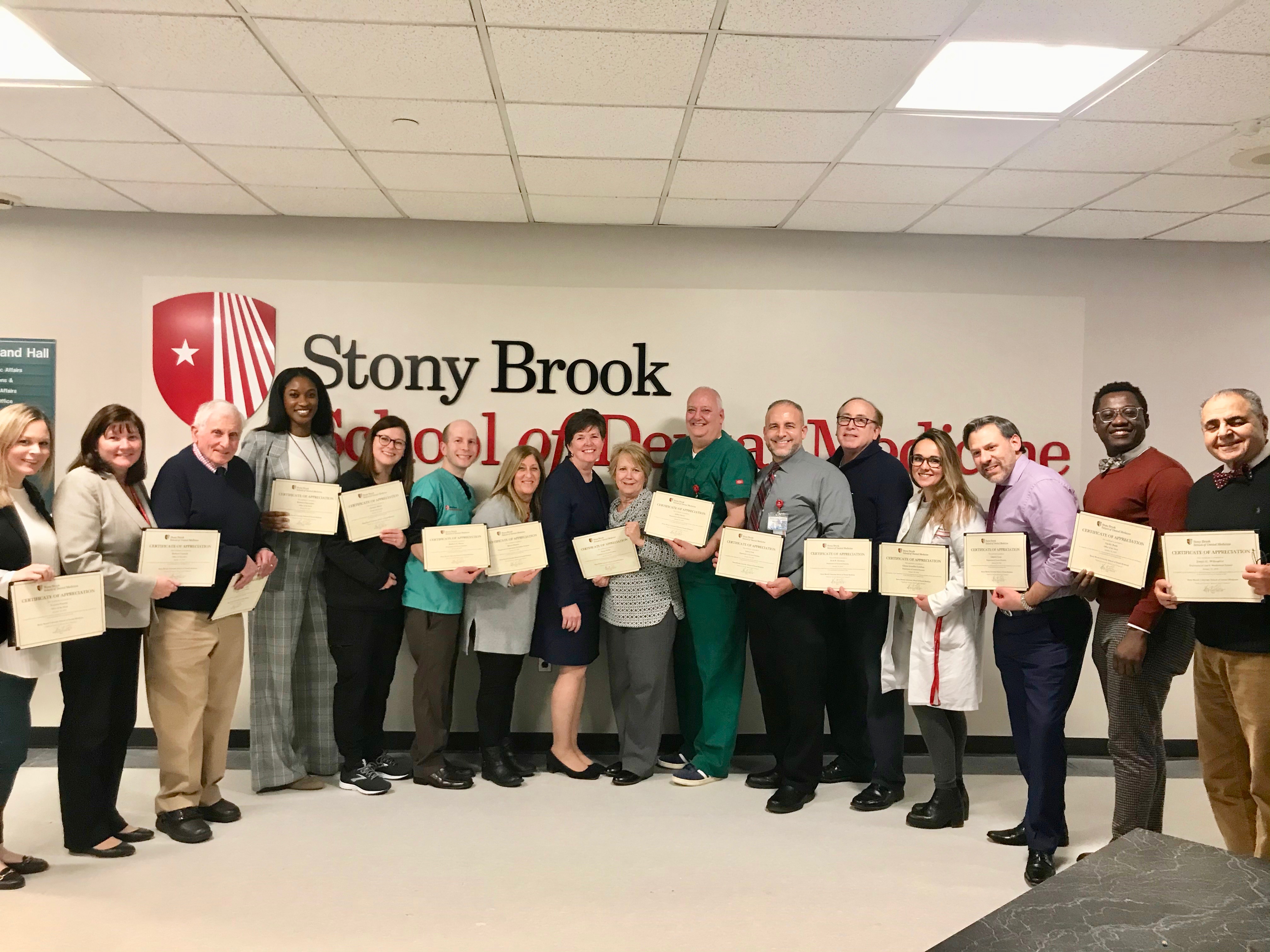 Group photo of Stony Brook School of Dental Medicine faculty and staff holding award certificates. 