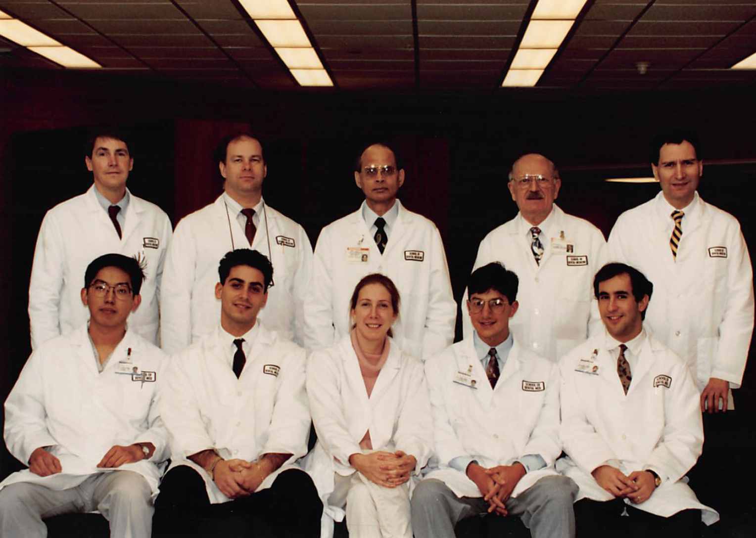 A group photo with one row of people standing and another row sitting in front. Everyone is wearing a white lab coat. In the photo are members of the original class of Stony Brook School of Dental Medicine's advanced education program in periodontics. 